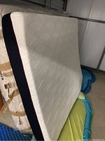 Foam mattress standing upright showing white patterned top surface, navy blue sides, and red trim.