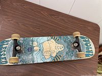 Full view of skateboard deck artwork showing Buddha figure and patterns with mounted wheels and trucks