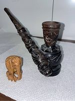Photo showing the dark carved wooden pipe next to the small blonde wood elephant figurine on a white paper towel background