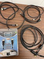 Four HDMI cables of varying lengths laid out on a wooden surface. One cable is in retail packaging labeled Vibe HDMI High Speed with Ethernet 5 ft (1.5 m). The other three cables are loose and unbranded.