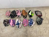 Overview of 12 kids leather baseball gloves in various colors and brands arranged on floor.