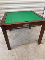 Front angle view of the wooden Lego table with the green baseplate on top, showing the Imaginarium and Lego brand labels on the side frame.