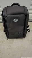 Front view of the black Nomatic backpack showing the rounded design with the Nomatic logo and the 'R' symbol.