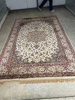 Full view of rectangular cream background area rug with medallion and floral border laid on concrete floor