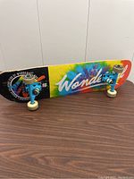 Side view of the skateboard showing tie-dye pattern and branding