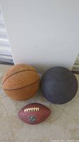 Photo showing Rawlings brown basketball, Spalding black basketball, and Wilson NFL football on floor against white background.