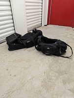 Two black duffle bags on concrete floor near red door, showing overall size and form.