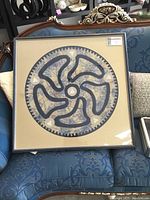 Full view of the framed textile artwork displayed on a blue patterned sofa, showing its large size and professional framing.