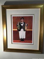 Gold framed colorful lithograph showing a waiter with a bottle of wine and a fish, signature visible