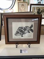 Framed artwork of an ink drawing of a fish titled "Maccjack Cottage" on display, showing overall lot contents and frame.