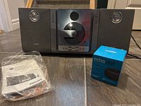 Photo showing Philips MCM-240 stereo system with two attached speakers and user manual, alongside new boxed Amazon Echo Dot
