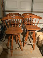 Four maple captain style swivel bar stools with turned spindles and metal foot rests in a garage setting.