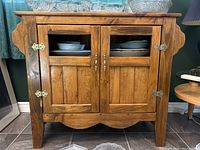 Front view of closed two-door varnished wooden cabinet with glass panels in doors, showing scratches and some wear.