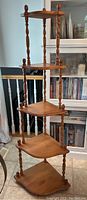 Full view of the four-tier wooden corner what-not shelf with turned spindles and shaped triangular shelves against a home interior background.