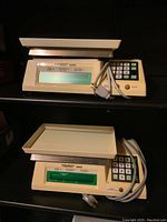 Two Toledo Model 8430 digital commercial scales on a shelf, each with tray, numeric keypad and power cords visible.