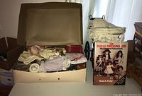 Box of doll making supplies including cloth dolls parts, doll wigs, doll clothes, and doll eyes, shown inside an open cardboard box.
