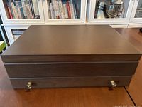 Closed mahogany-colored wooden box with brass knob handles, housing the cutlery.