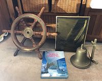 Full view of the four nautical items grouped with the ship wheel, book, brass bell, and framed etching visible.