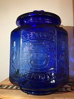 Front angle showing embossed Planters Pennant Peanuts with 5¢ symbol on cobalt blue glass jar