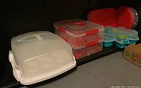 All containers grouped on shelf including red two-layer cupcake holders, white rectangular container, and clear flower-shaped container