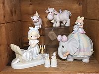 Eleven Precious Moments figurines displayed on wooden shelves, showing animals and children figurines with a general view of the lot contents