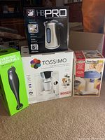 Overview of all four appliances in their original packaging: HB Pro digital kettle, Tassimo coffee brewer, Rival snow cone maker, Everyday Essentials hand blender.