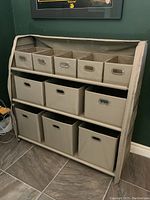 Front view showing three shelves each filled with collapsible fabric bins, metal handles on some bins, in beige color.