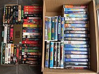 Two boxes of VHS tapes arranged side by side, showing a variety of movies including Star Wars Trilogy Special Edition, Disney cartoons, family and action movies.