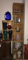 Photo showing eight wooden crates stacked with various decorative glassware and pottery inside and on top.
