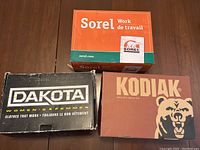 Three branded boot boxes for Sorel, Dakota, and Kodiak placed side by side on a table, showing original packaging and logos.