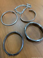 Top view of five silver bracelets laid out on a wooden surface showing their different styles and sizes.