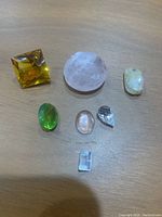Overview of seven loose gemstones displayed on a wooden surface, showing variety of sizes, cuts and colours.