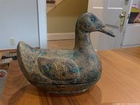 Side angle showing full duck shape, textured body, and patina on cast iron dish with lid.