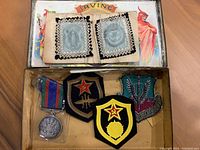Collection including badges with religious imagery, shield-shaped military patches, and silver medal inside Irving Cigar Box