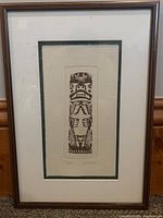 Framed etching depicting the totem pole figure, showing full artwork and frame, hung against a wall