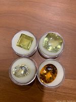 Four loose lemon citrine gemstones in individual round containers showing variety of cuts and colors.