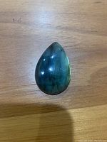Top-down view of pear shaped labradorite gemstone showing blue-green iridescence and polished surface.