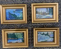 Four framed miniature paintings arranged in a 2x2 grid on a dark carpet, showing landscape scenes with water, trees, and rocky outcrops.