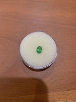 Oval green Tsavorite loose gemstone on a round foam holder on wood surface.