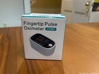 Front and side view of the boxed fingertip pulse oximeter model X1907 showing the device image and product name.