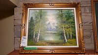 Front view of the framed landscape canvas painting with birch trees, lake, and mountains signed R. Thomas.