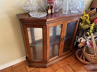 Front-facing view of the Craftline cabinet showing glass doors, wooden frame and items placed on top for size context.