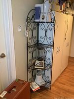 Full view of black metal corner shelf placed in corner of a room near cabinets. Several kitchen appliances are shown sitting on the shelves but are not included in the sale.