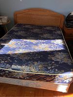 Full or double bed with oak wood finish headboard, blue floral mattress on metal frame