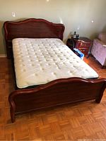 Full view of the double bed with wood headboard and footboard, mattress on top, showing bed design and finish.