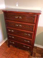 Front view of the wooden dresser showing five drawers with brass handles and reddish-brown frame.
