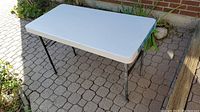 Folded white Lifetime table with black legs visible underneath, photographed outside on a paved surface.
