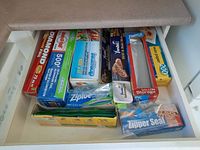 Drawer containing boxes of aluminum foil, Ziploc bags, wax paper, and seal wrap stored neatly for food storage and kitchen use.