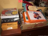 Two boxed board games, a wooden box of dominos, and a cardboard box with craft supplies