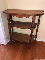 Front view of three tiered wooden hall table with carved turned legs and scalloped edges on shelves.